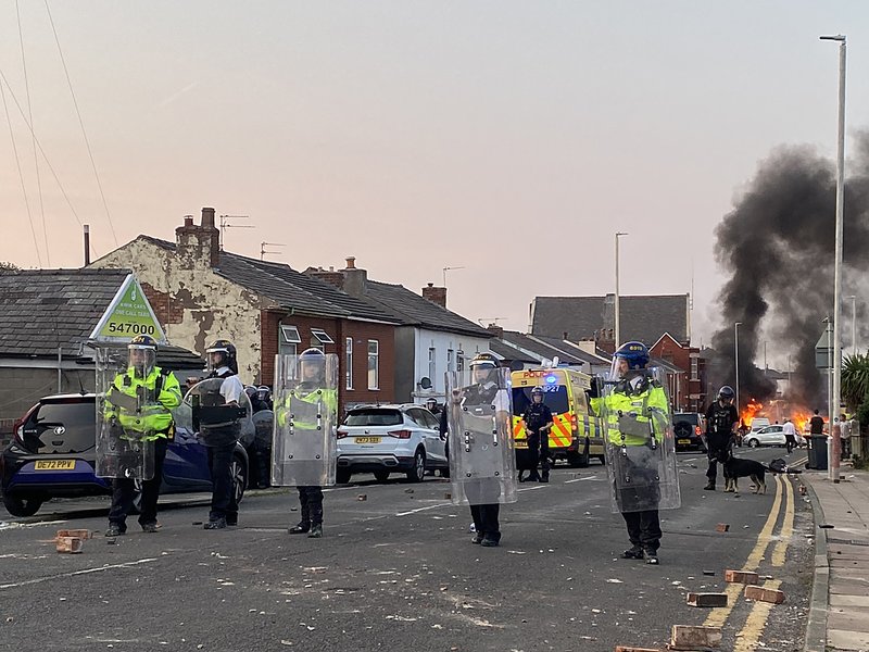 Smoke billows from a fire started by protesters as riot police stand guard after disturbances near the Southport Islamic Society Mosque in Southport, northwest England, on July 30, 2024, a day after a deadly child knife attack